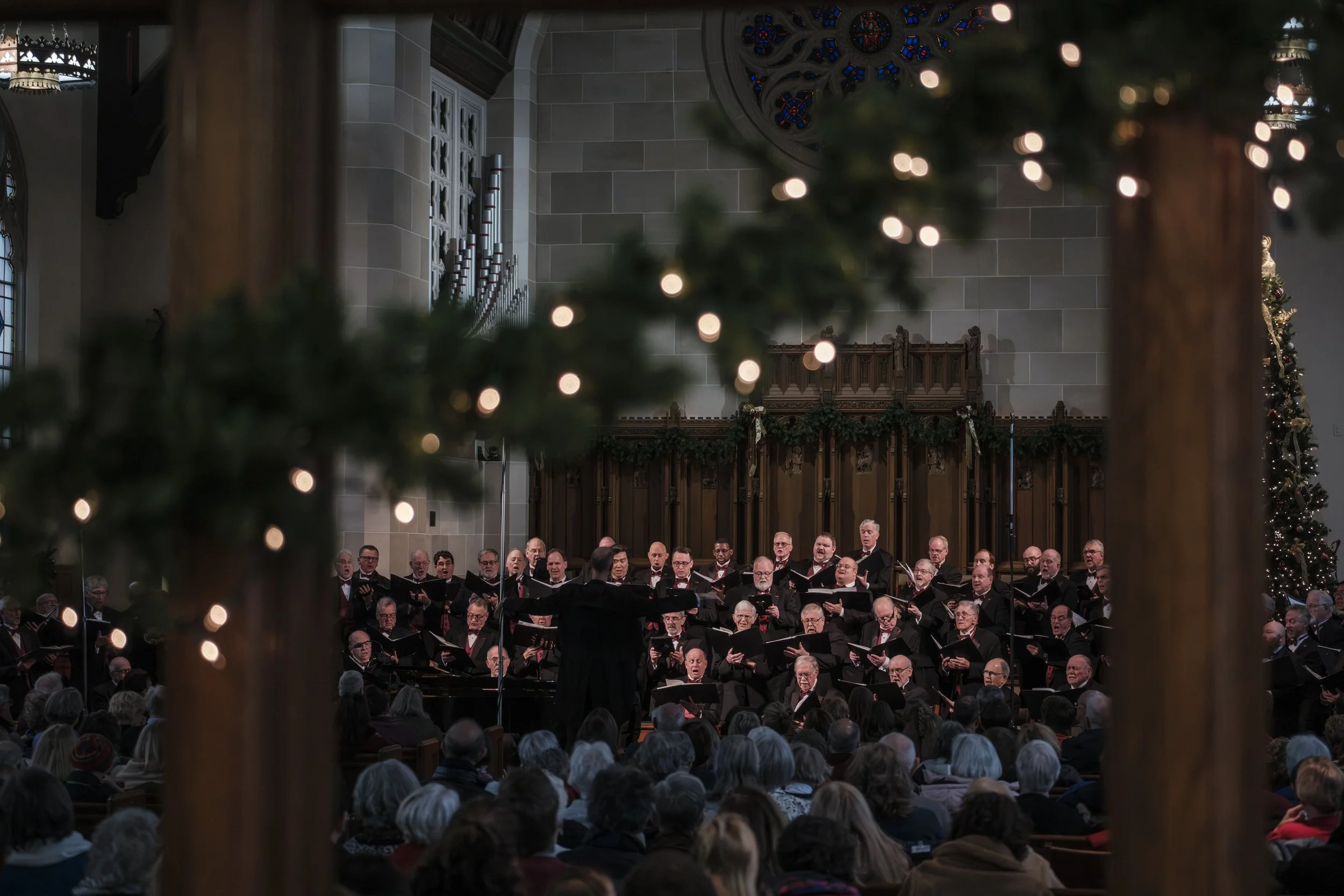 The Measure for Measure men's choir sings on stage, framed between Christmas decor during their Sounds of the Season holiday concert