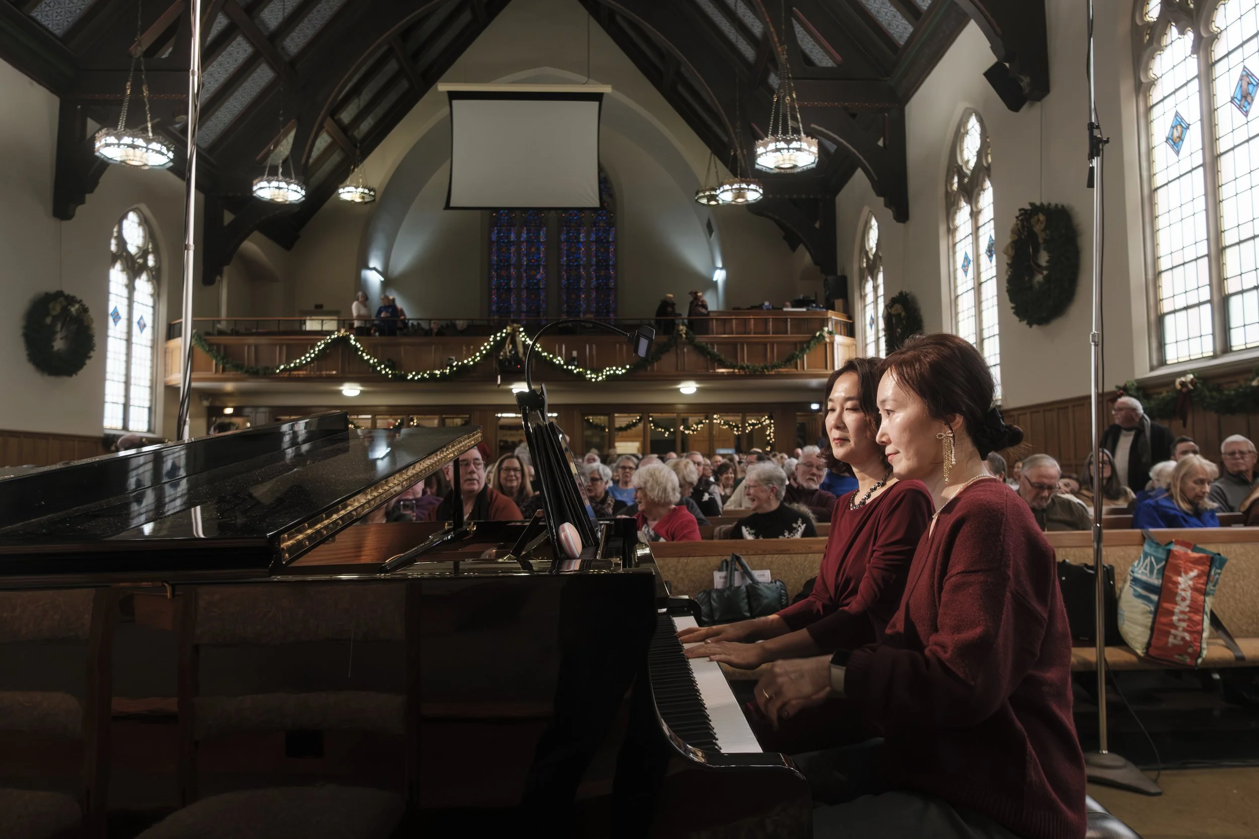 Two piano players play on stage at the First United Methodist Church of Ann Arbor while the audience filters in