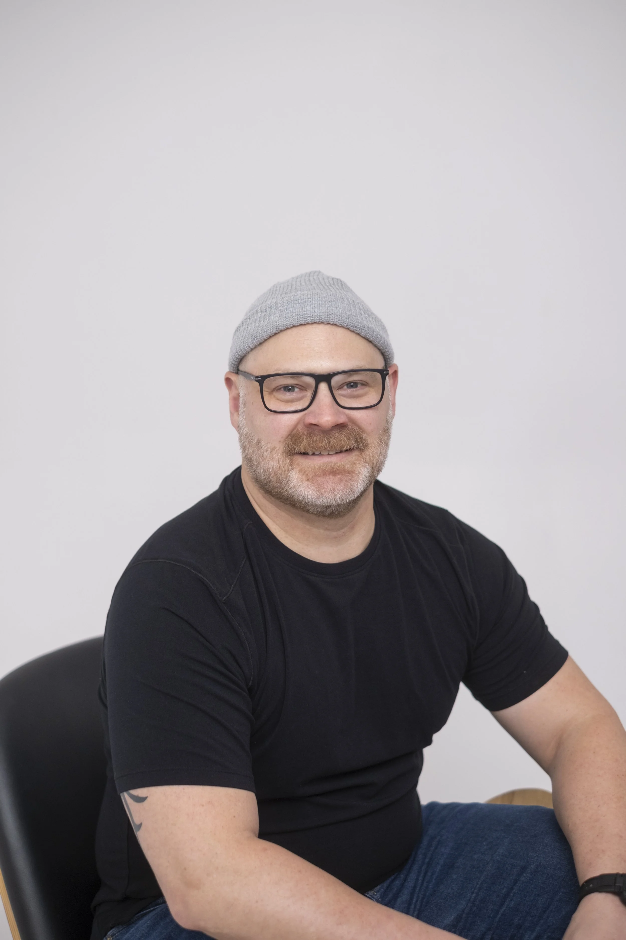 A posed photo of a man wearing a beanie and glasses at StudioStudio, a studio in Ann Arbor, Michigan