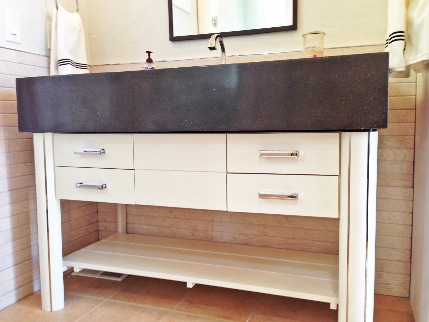 The vanity is designed with an open shelf bottom, to store rolled-up towels for guests. Four drawers provide nice storage. The legs are 4" in diameter and have polished chrome inlays running from top to bottom. My favorite part of this piece is the 8" thick concrete countertop that rests on top of the vanity. It has an integrated trough sink. Brizo Virage Faucet and sconces. 
