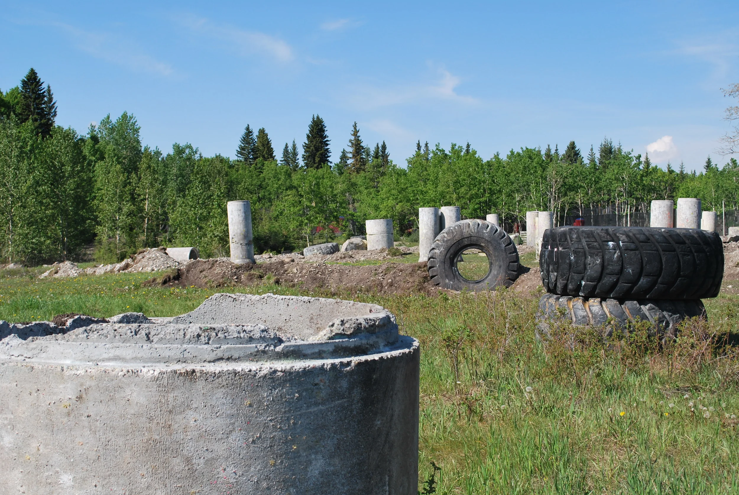 Outdoor obstacle course with stacked tires and concrete pillars in a grassy field surrounded by trees.