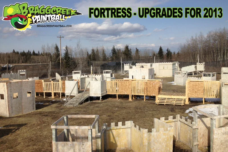 Outdoor paintball field at Bragg Creek Paintball with fortress-like structures and upgrades for 2013, surrounded by trees and clear skies.