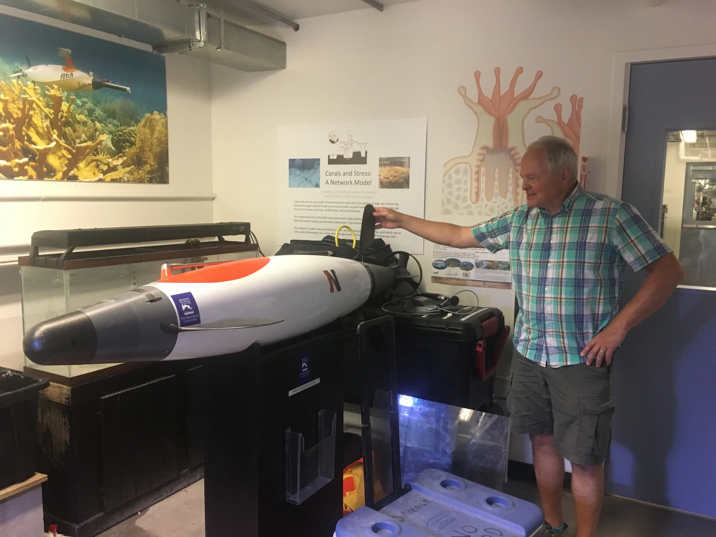 Mark Patterson with an AUV (Autonomous Underwater Vehicle). Fun Fact: the poster in the back of this photo shows the longest continuously running underwater robot (AUV)! 