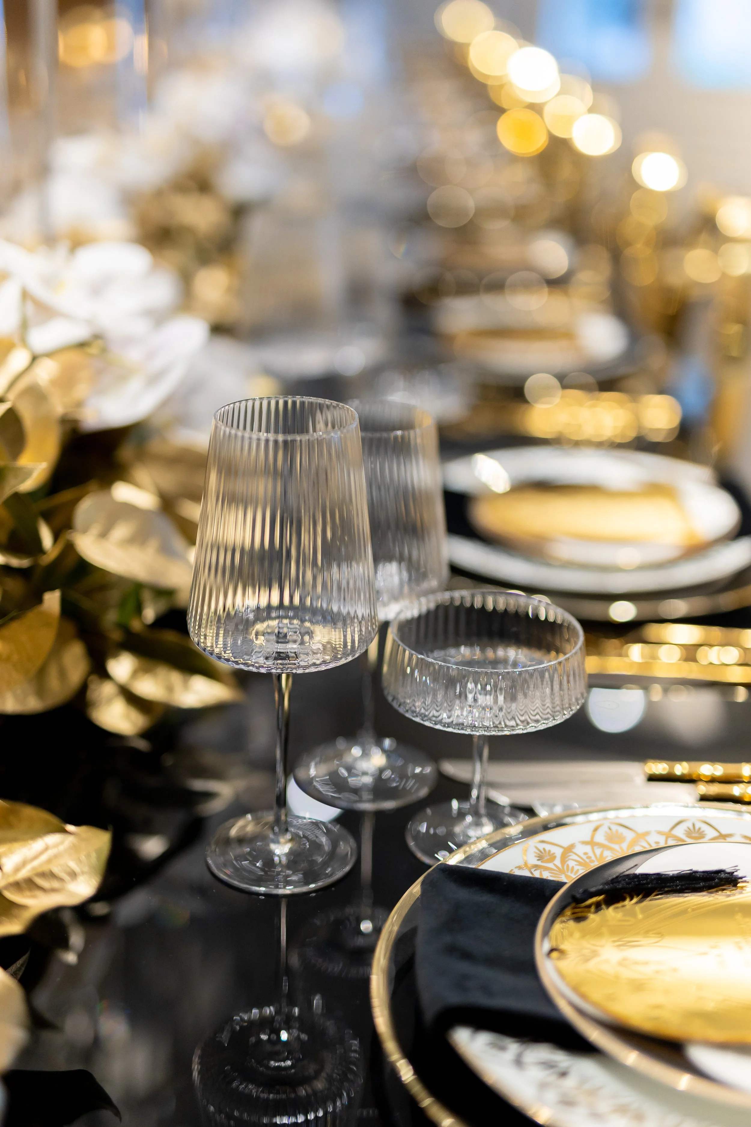 Elegant table setting with gold and black accents, crystal glasses, floral centerpiece, and fine china at a formal event.
