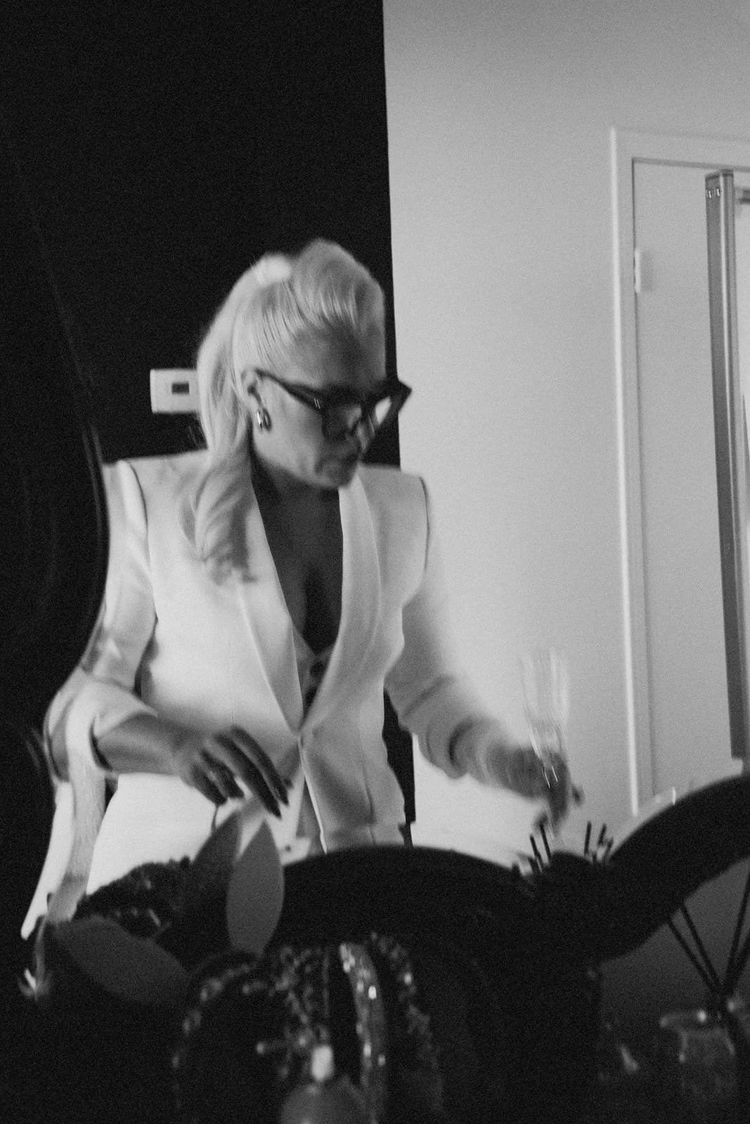 A woman with blonde hair and glasses is pouring a drink at a social event.