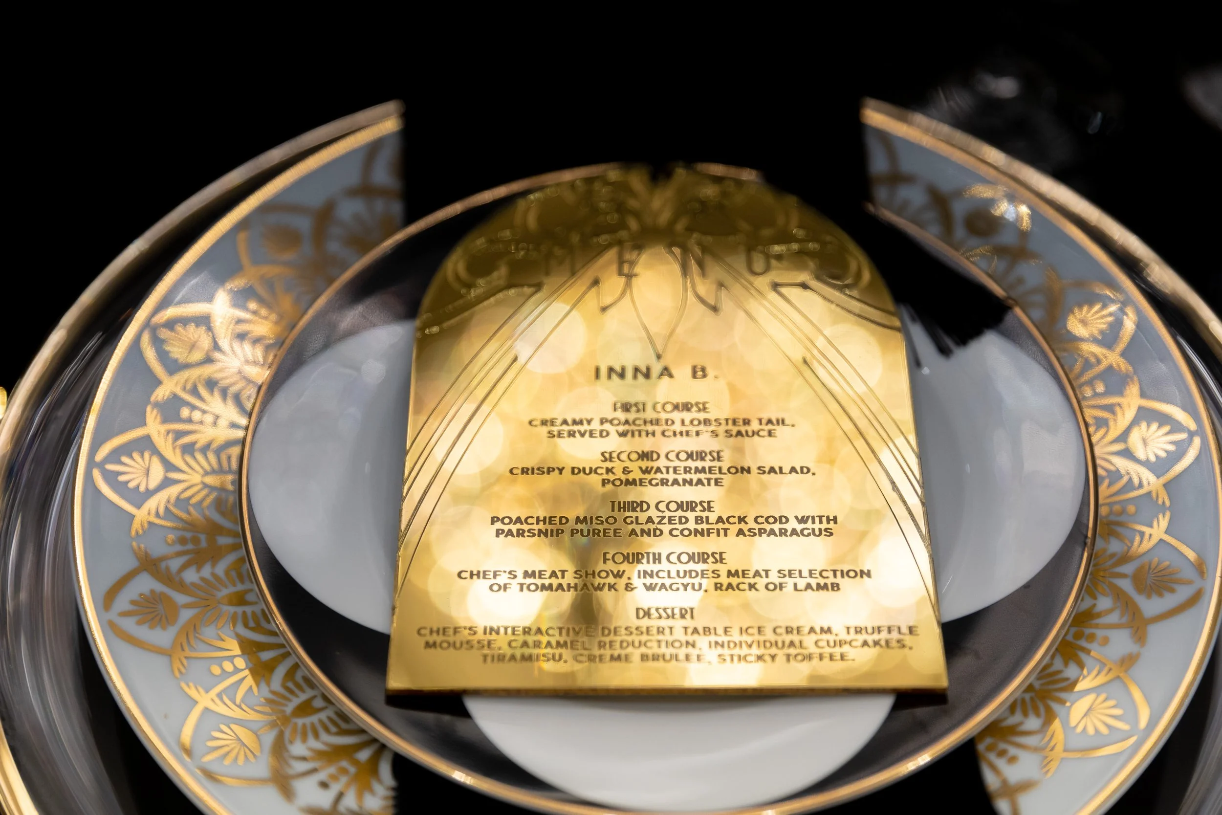 Elegant gold and black magazine or menu card with gold floral border, listing four courses and dessert options.