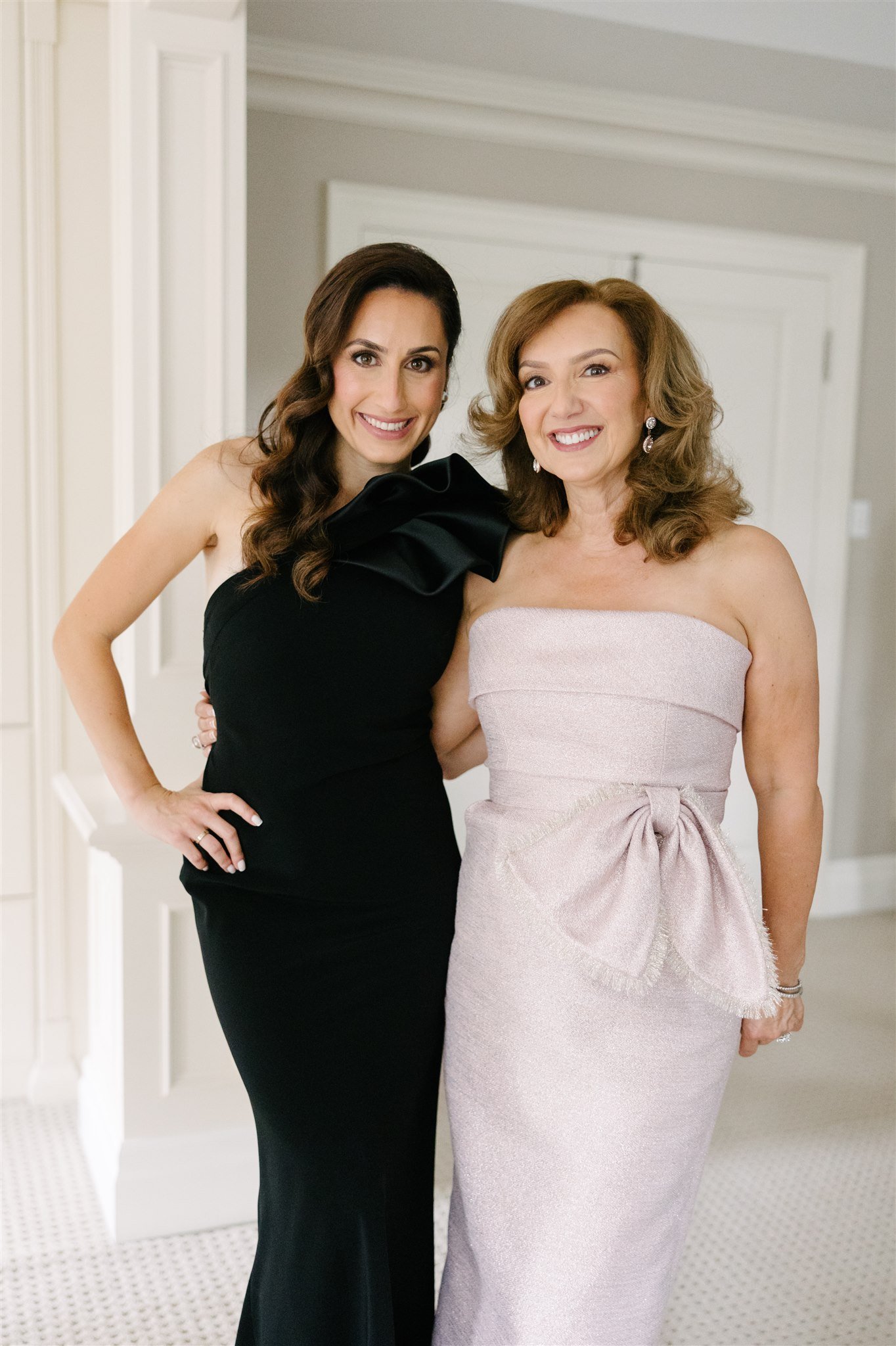 Two women in formal dresses smiling and posing together indoors.