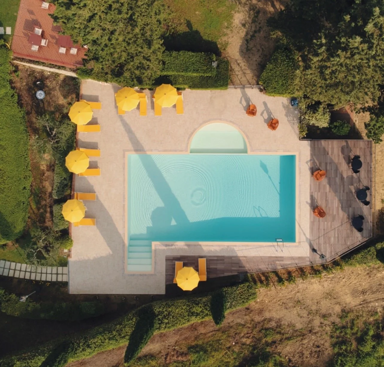 An aerial view of a swimming pool area with yellow umbrellas, lounge chairs, and trees surrounding it.