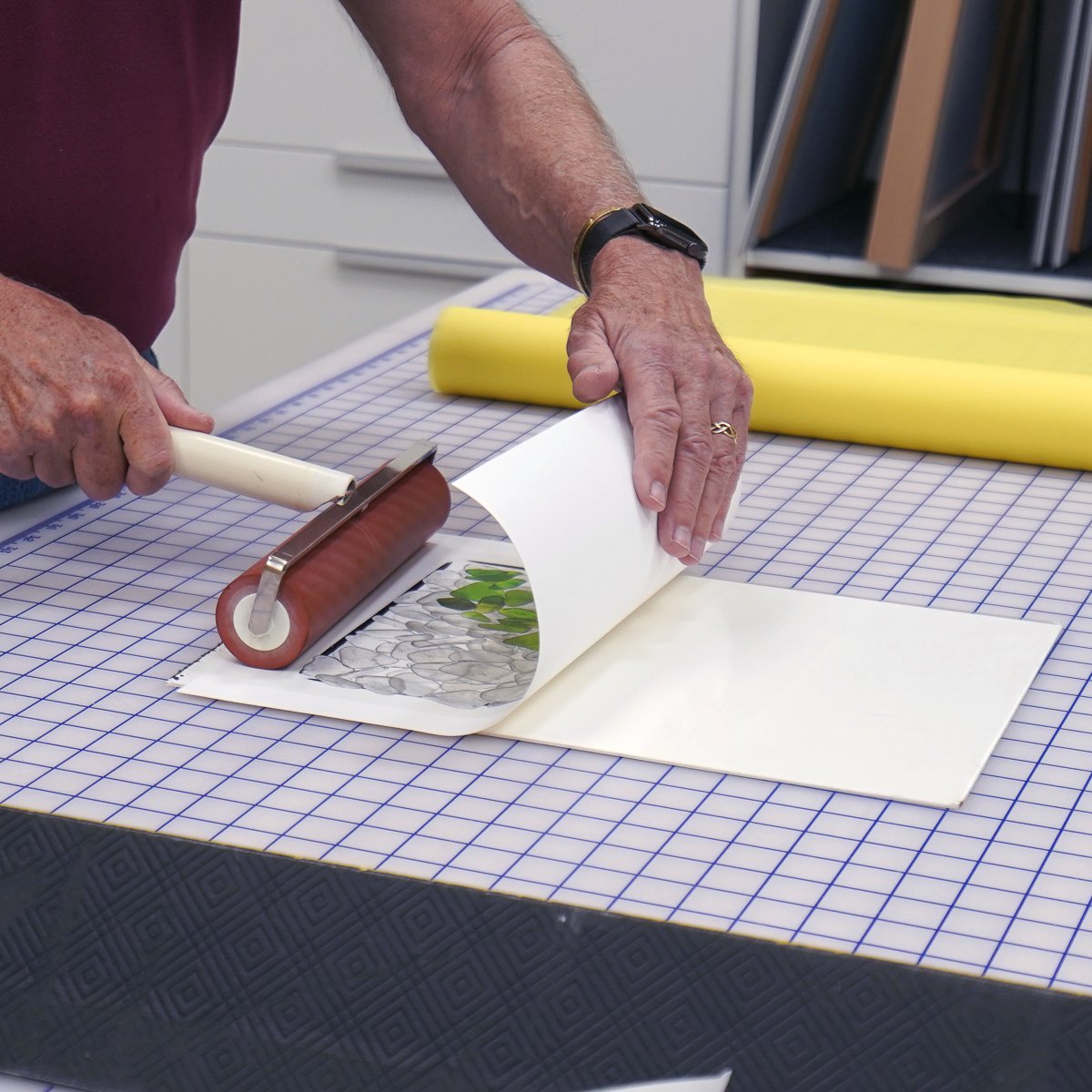  Then the print gets firmly rolled onto the adhesive with the brayer. Note how the print is kept curved as it’s pressed down. This way any unevenness in the print will be straightened. The main thing is to be sure the print is fully adhered with no a