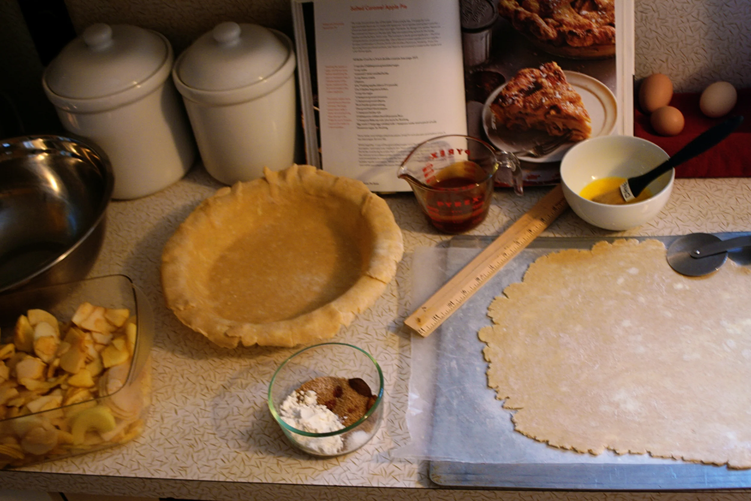 Here's a view of what I had ready for myself on day two thanks to day one's prep: apples, sliced and mixed with lemon and sugar; sugar-spice mixture; caramel, measured and ready to pour; pie dough that had been rolled out, half left on a sheet tray and popped into the freezer (only spot it fit) and one placed in the pie pan (kept in the fridge). 