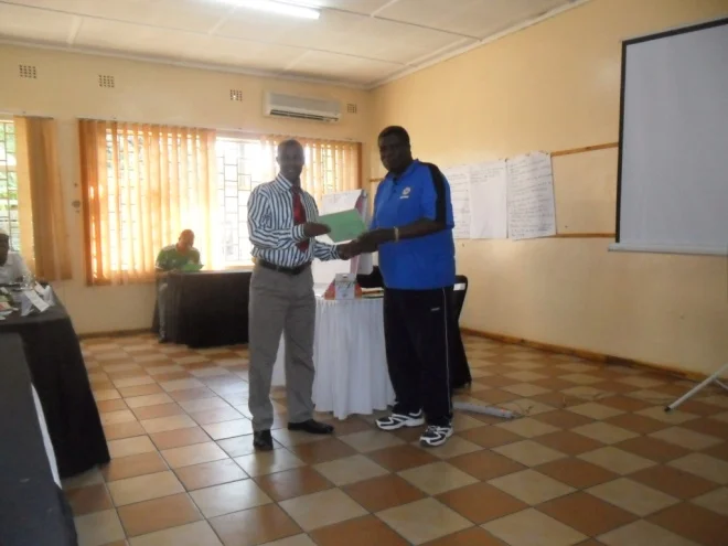 Mr. Isaac Mumba CHEP TB Programs Coordinator (in blue) presenting a Certificate of participation to Stanley Mulega (in white)