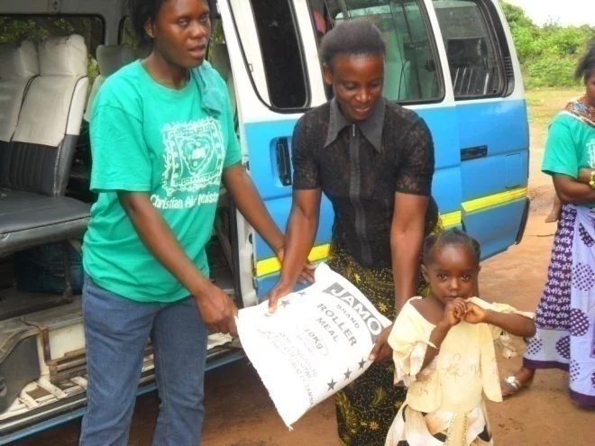 Matilda (in green) and Foster Yombwe CAM volunteers in St. Anthony and Kamakonde communities respectively giving food to Martha. Martha is three years old. She is HIV positive. She is one of the seven patients on ARVs and TB treatment in Kamakonde community who is on CAM monthly nutritional support program. Martha has recovered and she is looking healthy now