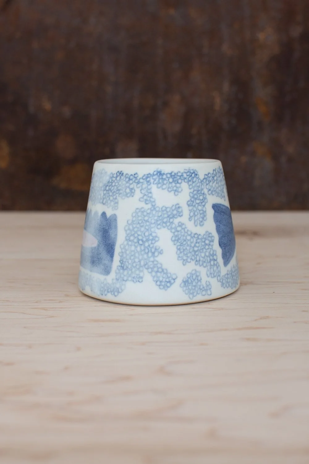 Hand-thrown porcelain mug with blue illustrations painted on the surface.