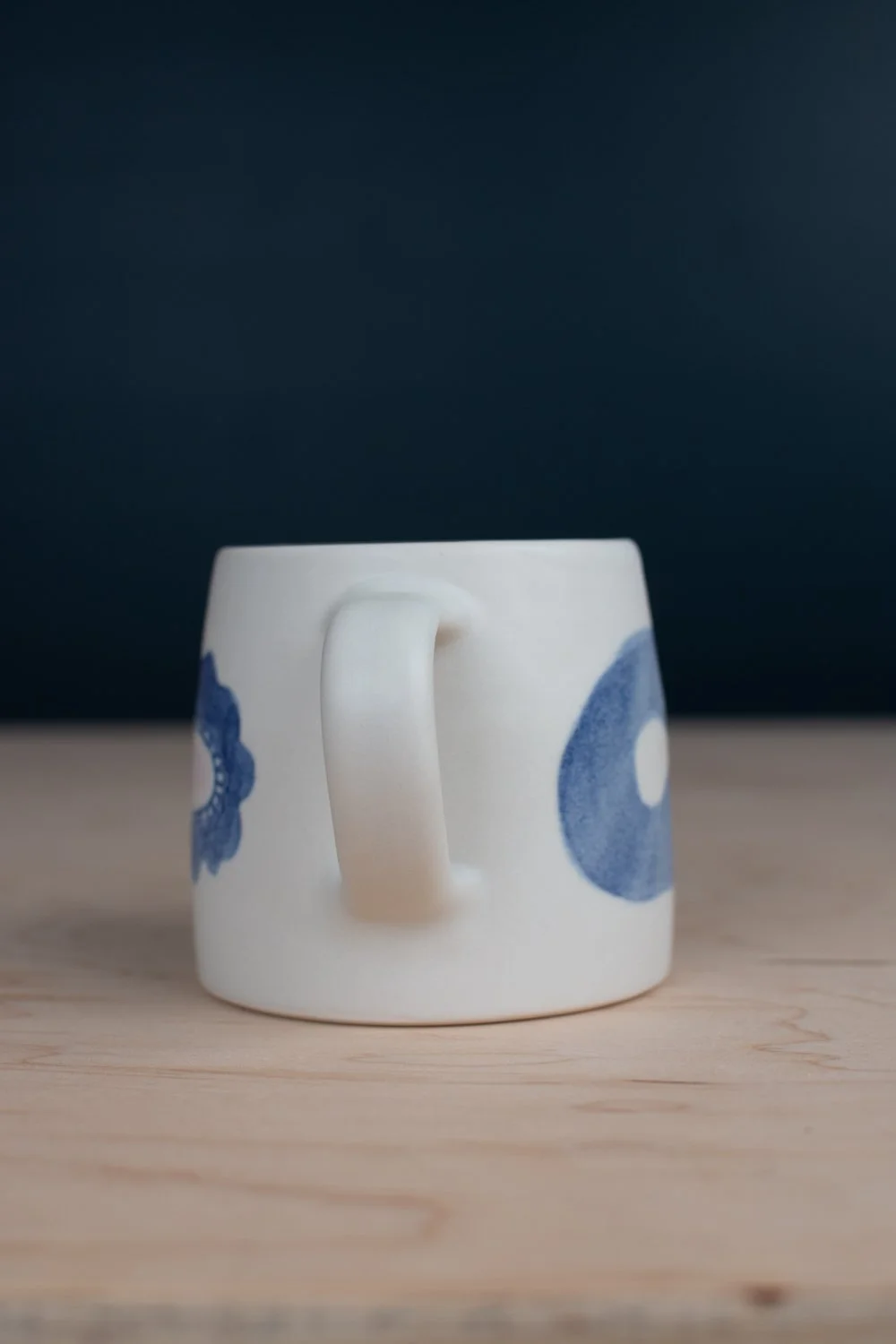 Hand-thrown porcelain mug with blue illustrations painted on the surface.