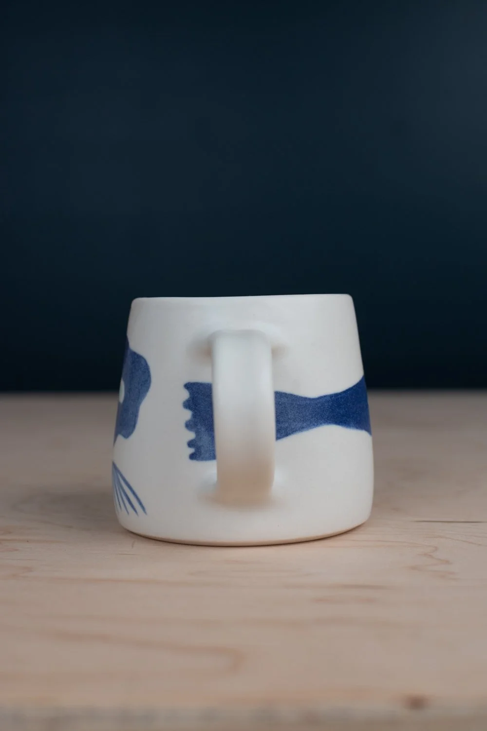 Hand-thrown porcelain mug with blue illustrations painted on the surface.