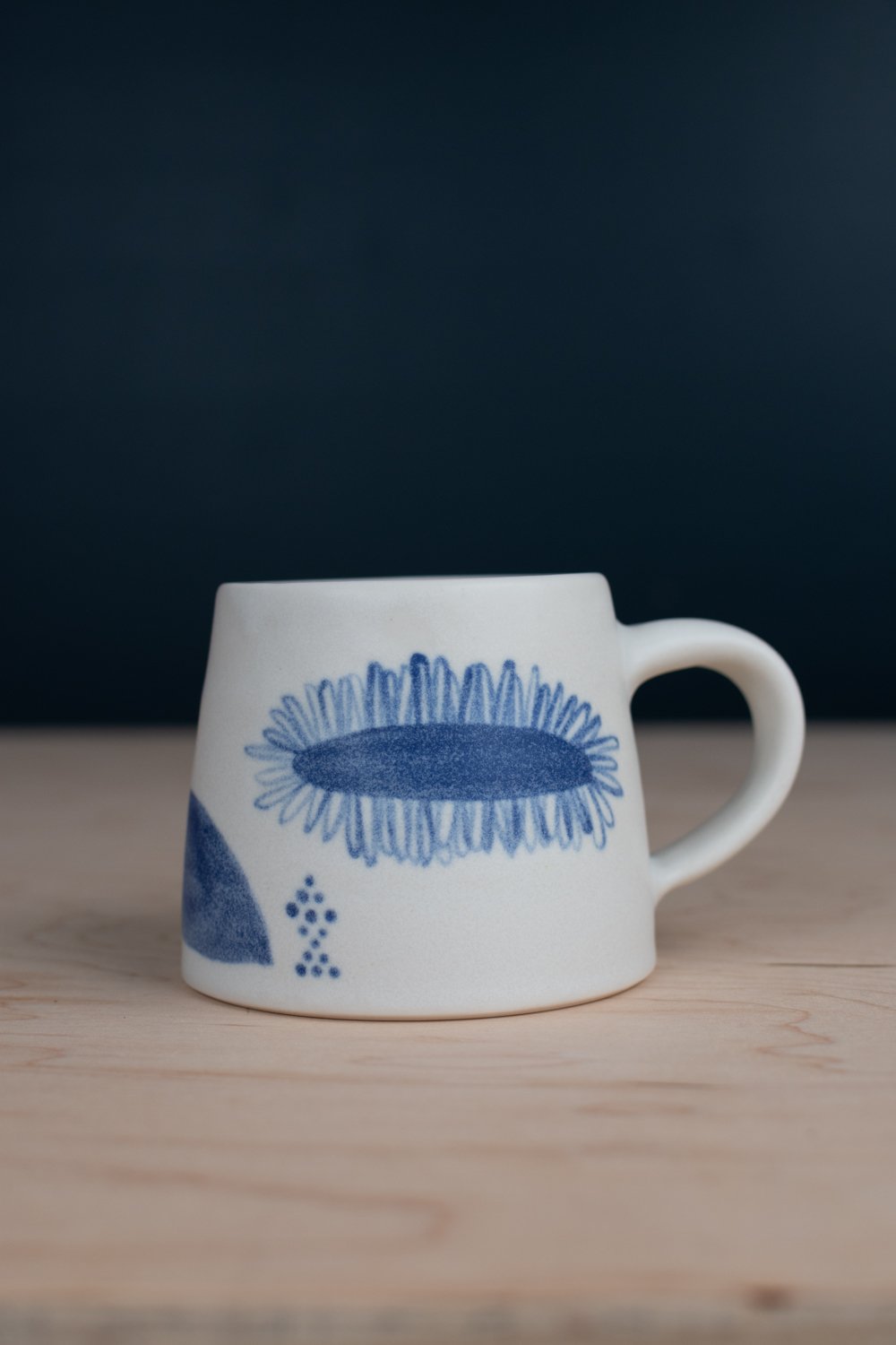Hand-thrown porcelain mug with blue illustrations painted on the surface.