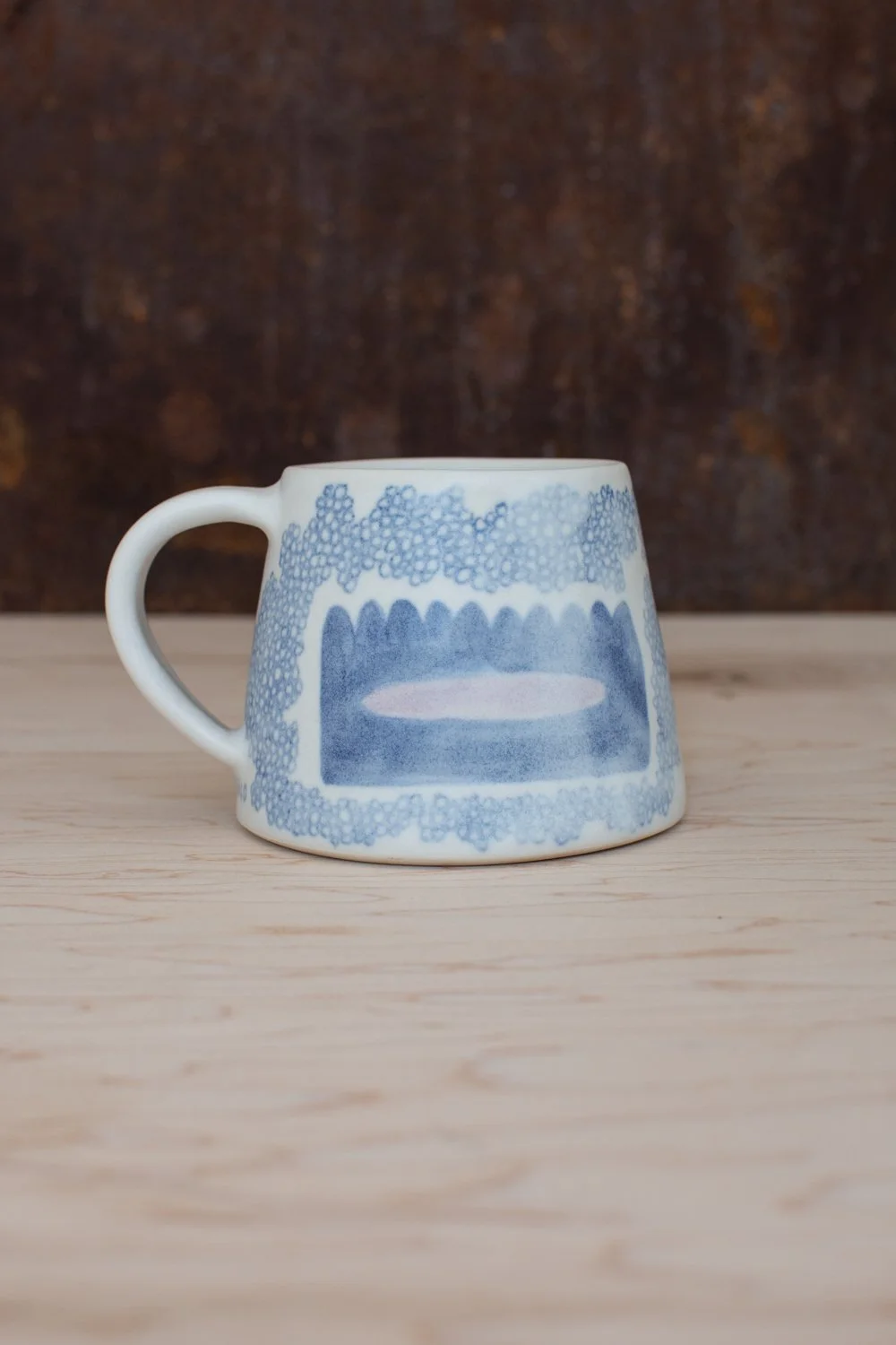 Hand-thrown porcelain mug with blue illustrations painted on the surface.