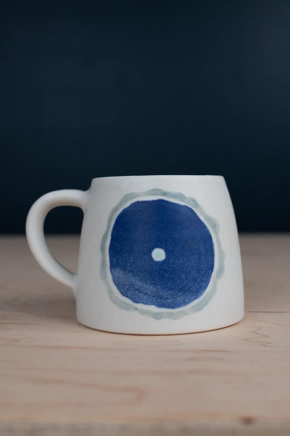 Hand-thrown porcelain mug with blue illustrations painted on the surface.
