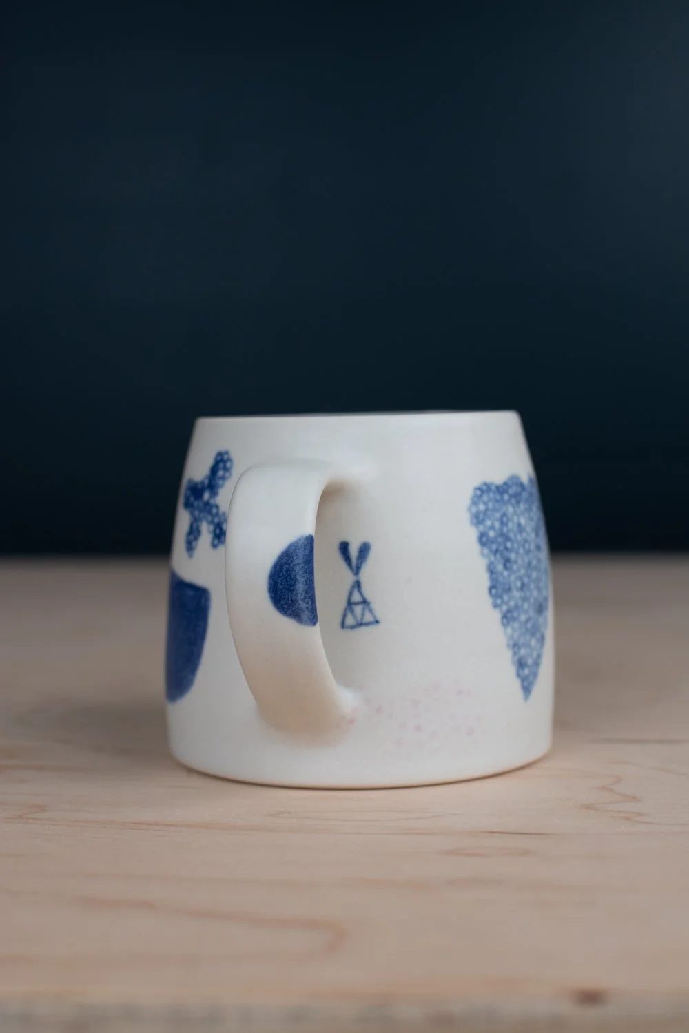 Hand-thrown porcelain mug with blue illustrations painted on the surface.