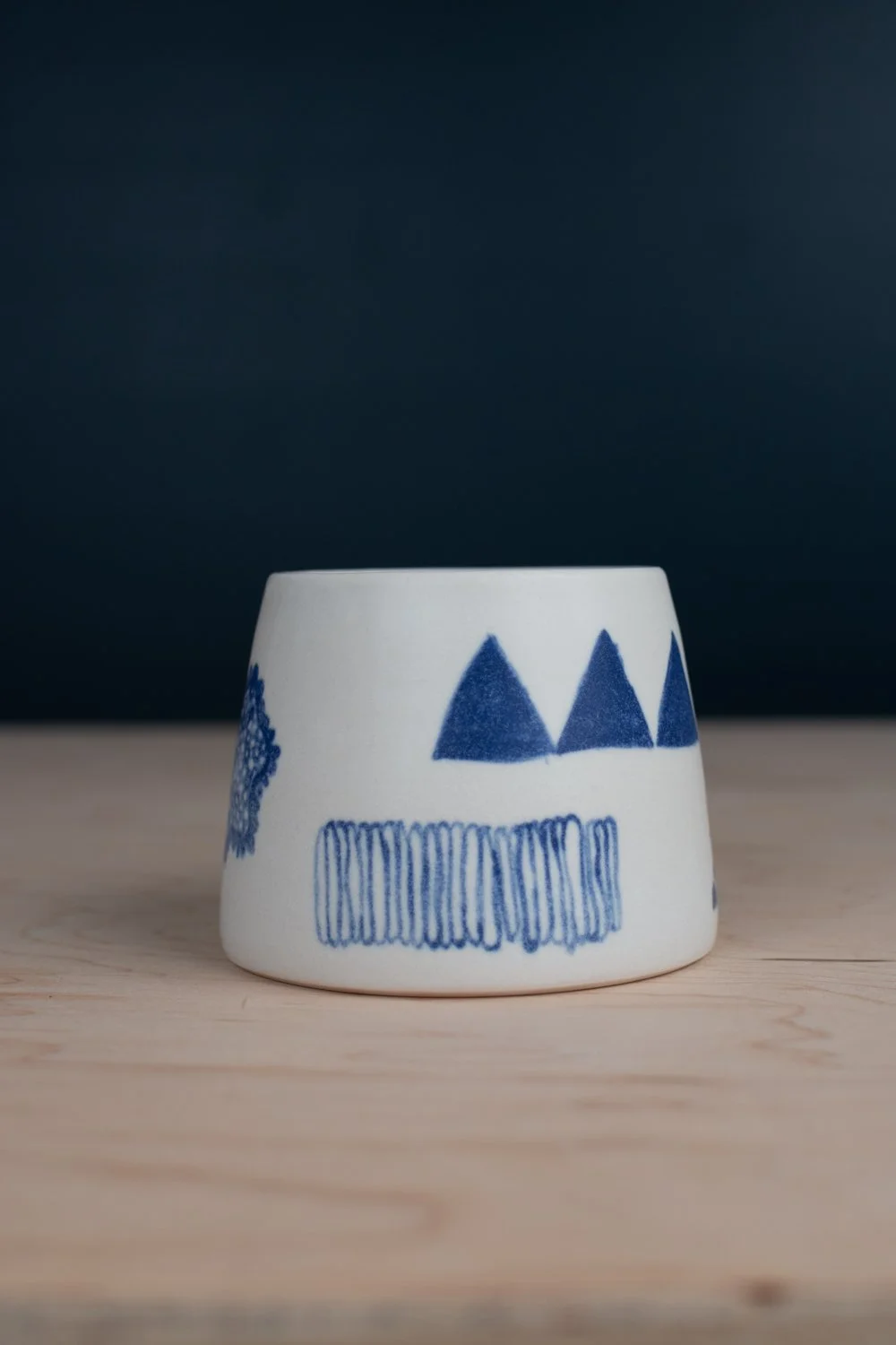 Hand-thrown porcelain mug with blue illustrations painted on the surface.