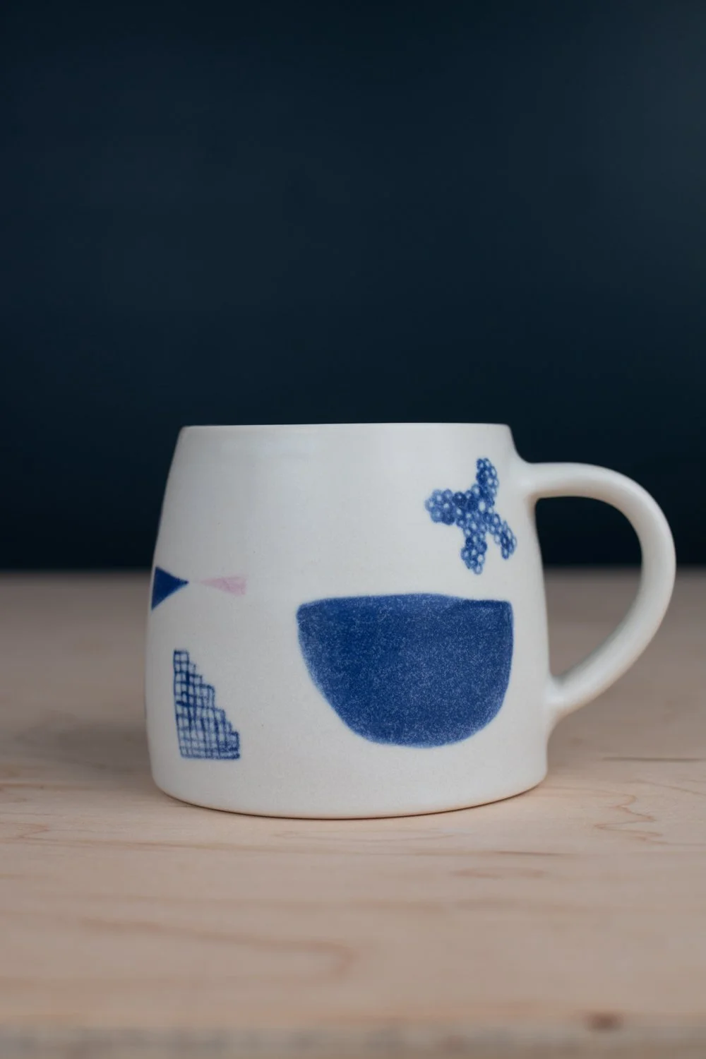 Hand-thrown porcelain mug with blue illustrations painted on the surface.
