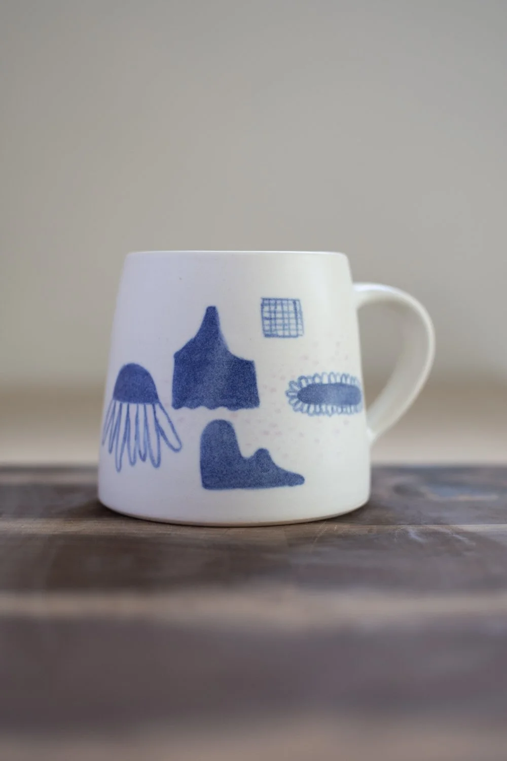 Hand-thrown porcelain mug with blue illustrations painted on the surface.