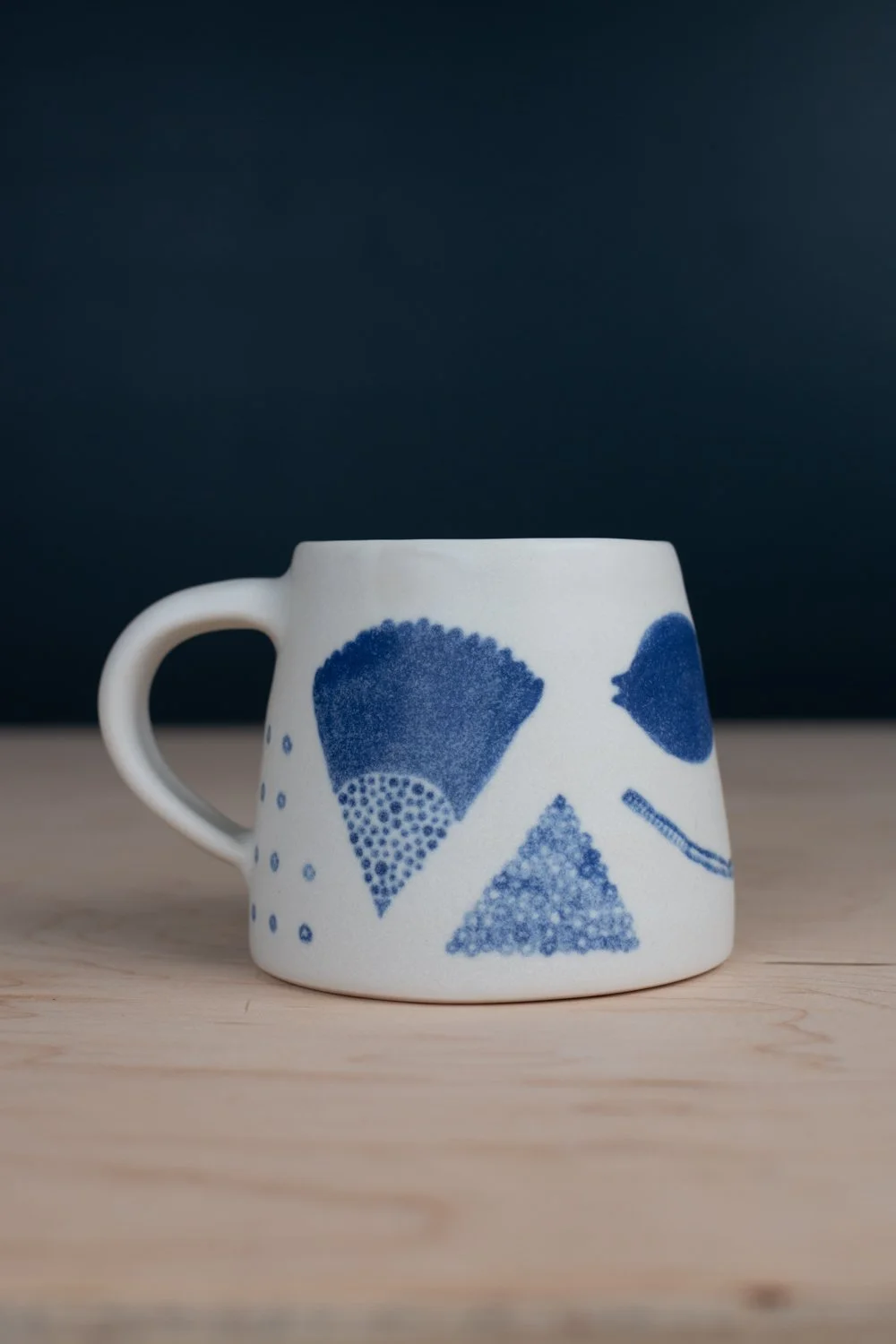 Hand-thrown porcelain mug with blue illustrations painted on the surface.