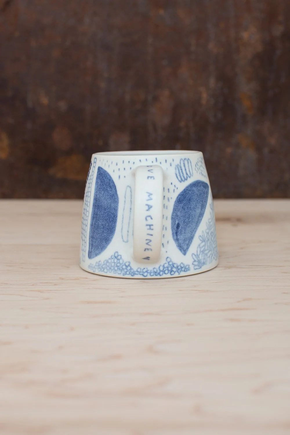 Hand-thrown porcelain mug with blue and pink illustrations painted on the surface.