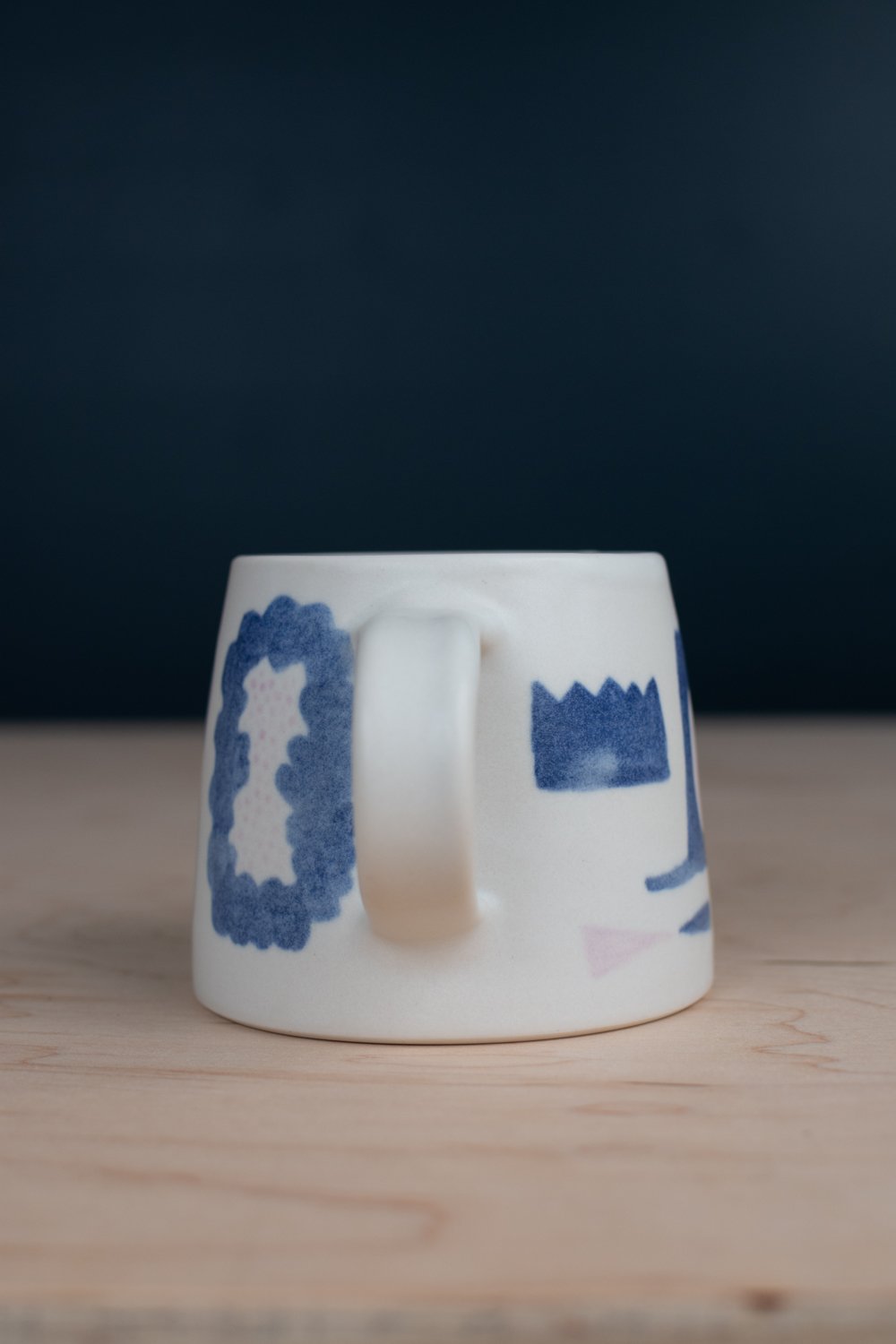 Hand-thrown porcelain mug with blue illustrations painted on the surface.