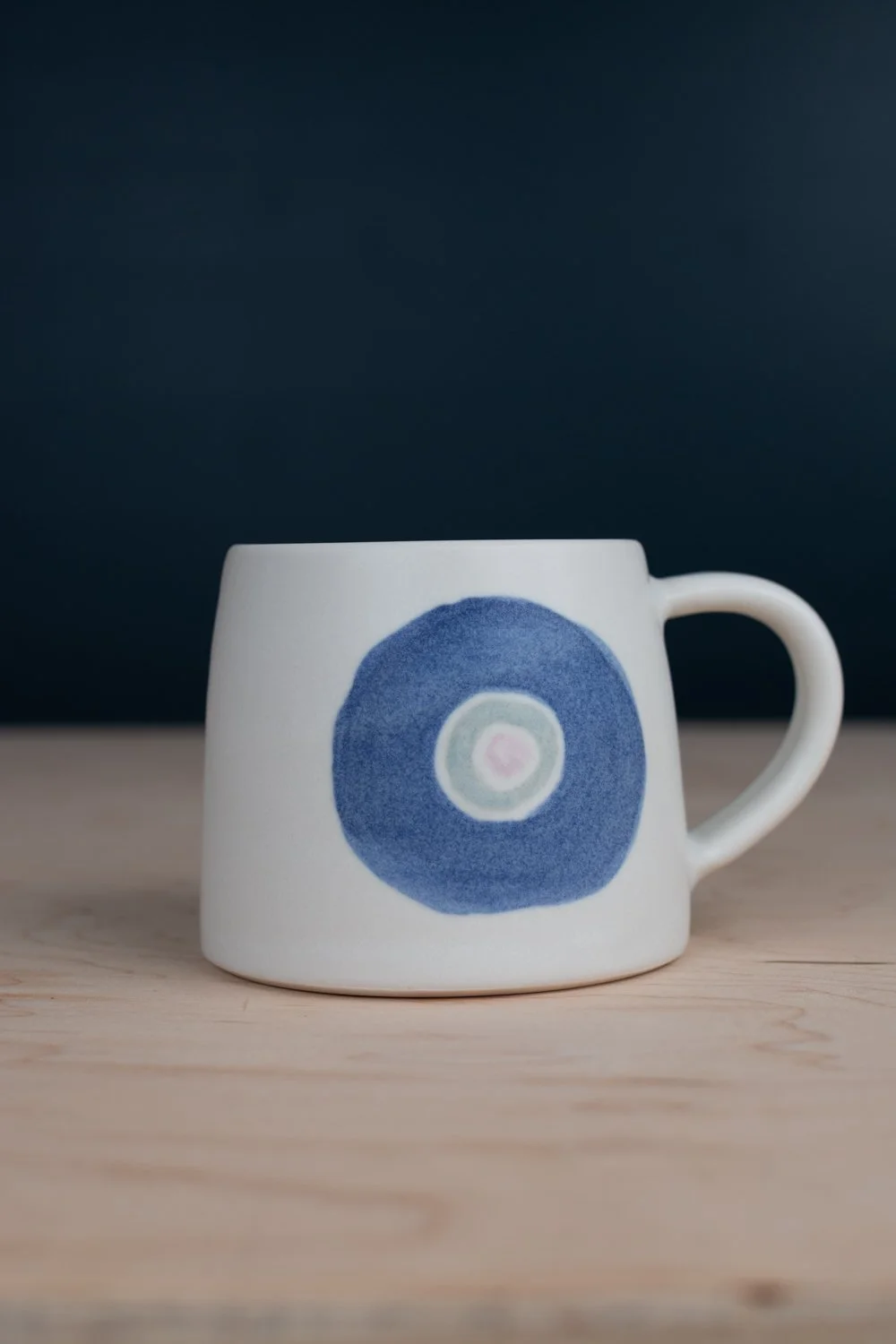 Hand-thrown porcelain mug with blue illustrations painted on the surface.