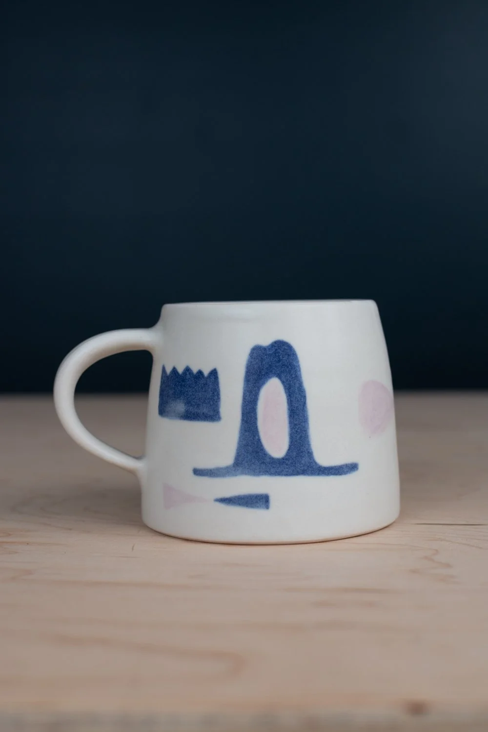 Hand-thrown porcelain mug with blue illustrations painted on the surface.