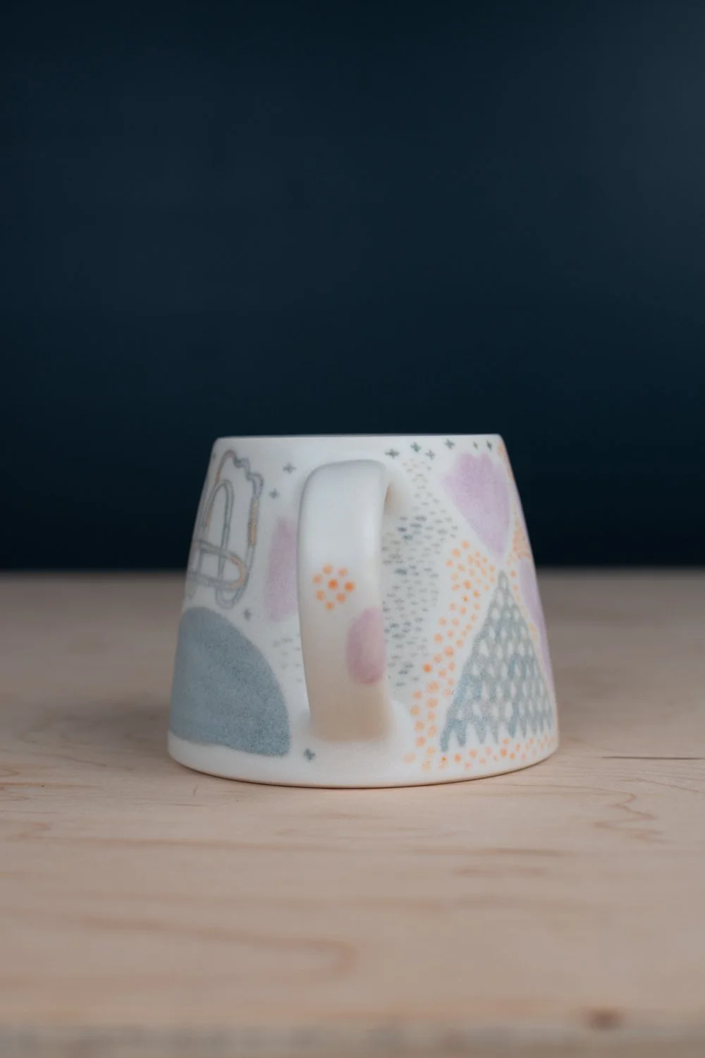 Hand-thrown porcelain mug with green, yellow, and lilac illustrations painted on the surface.