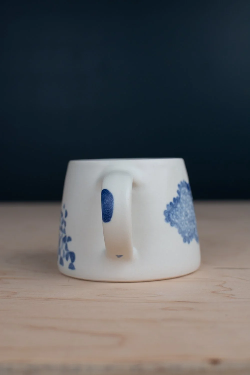 Hand-thrown porcelain mug with blue illustrations painted on the surface.