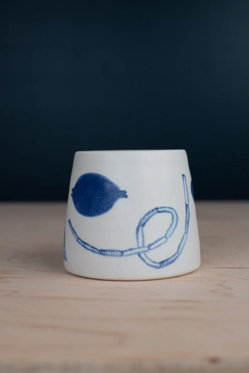 Hand-thrown porcelain mug with blue illustrations painted on the surface.