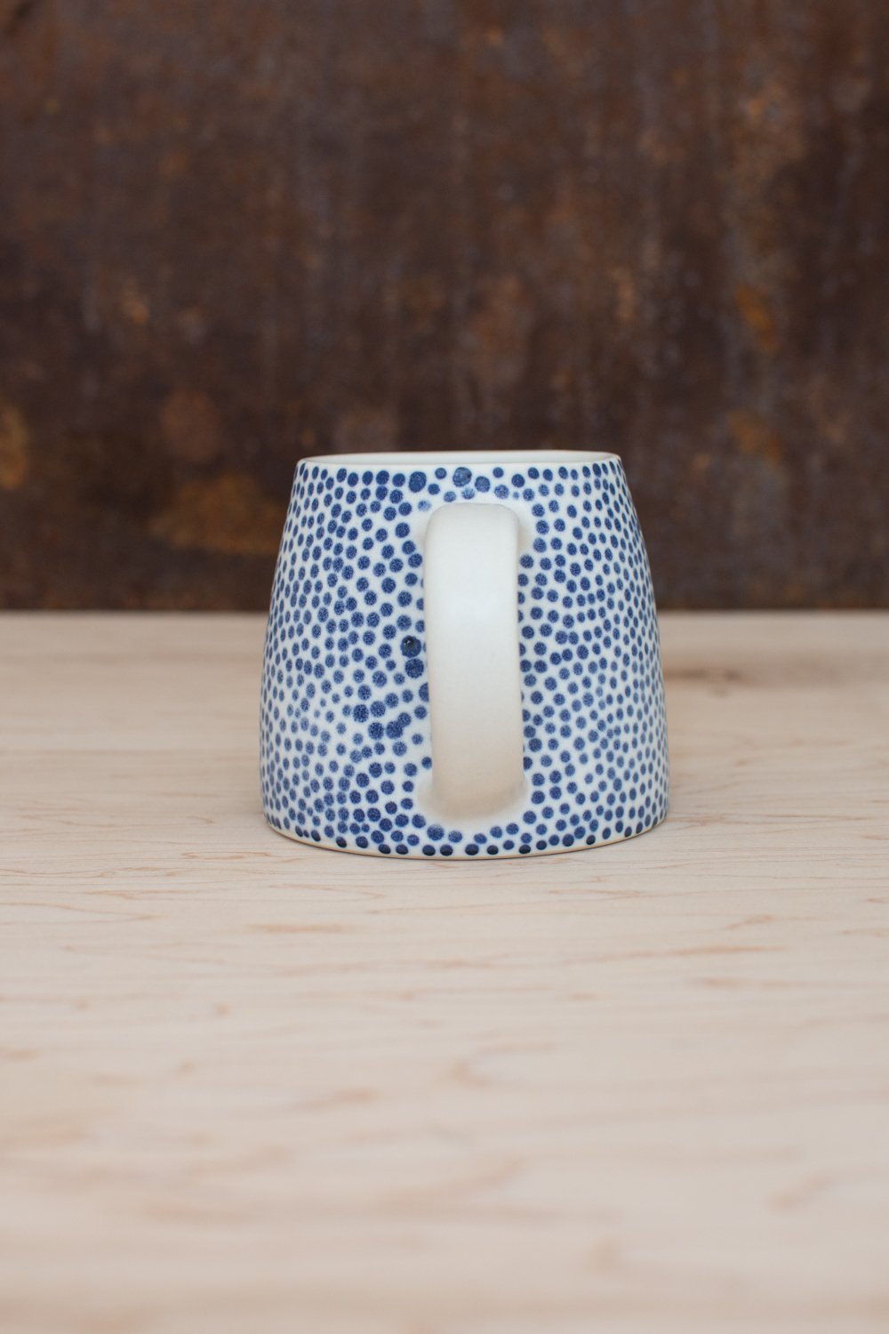 Hand-thrown porcelain mug with blue dots painted on the surface.