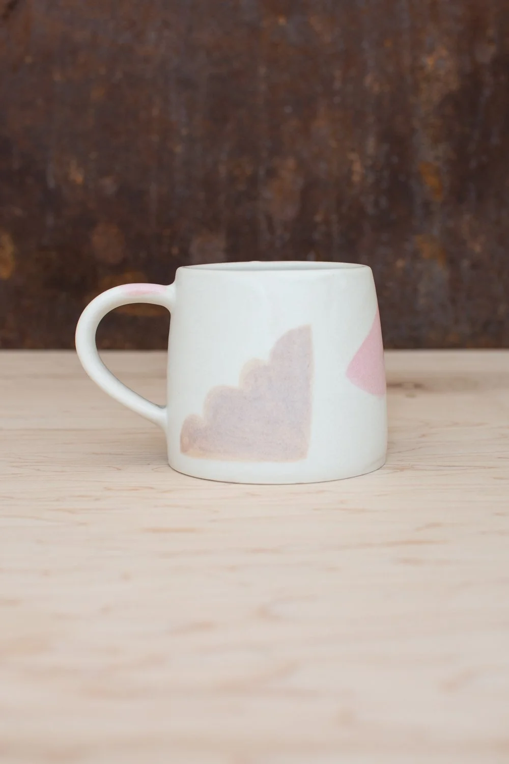 Hand-thrown porcelain mug with pink and ochre illustrations painted on the surface.