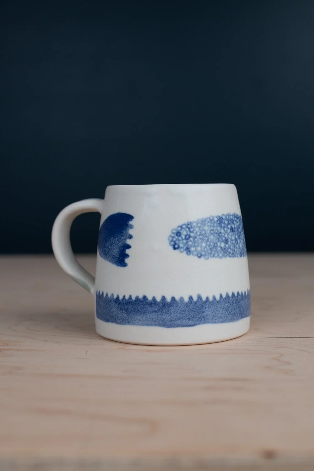 Hand-thrown porcelain mug with blue illustrations painted on the surface.