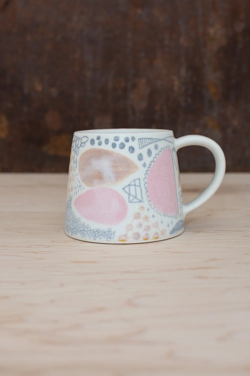Hand-thrown porcelain mug with pink and ochre illustrations painted on the surface.
