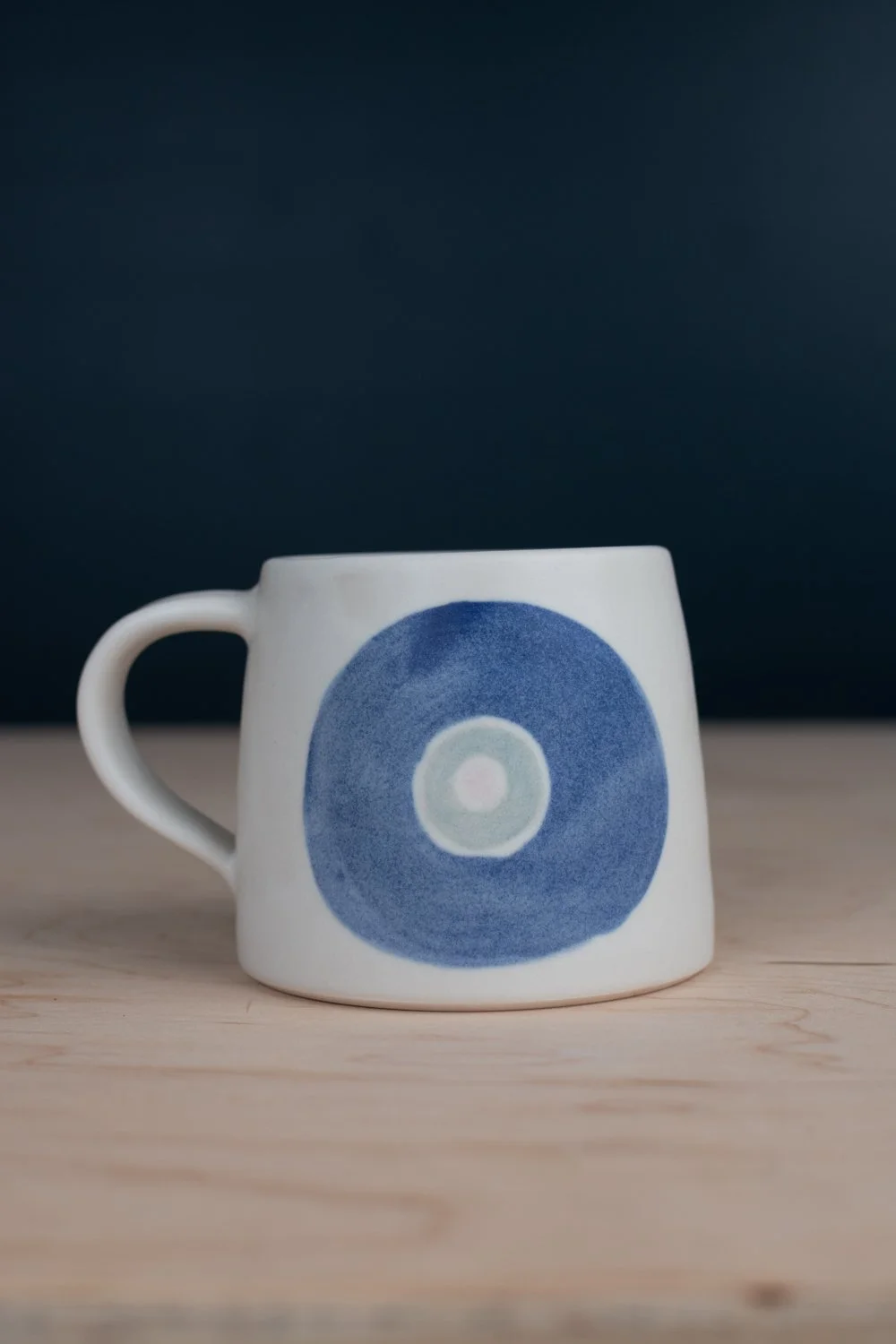 Hand-thrown porcelain mug with blue illustrations painted on the surface.
