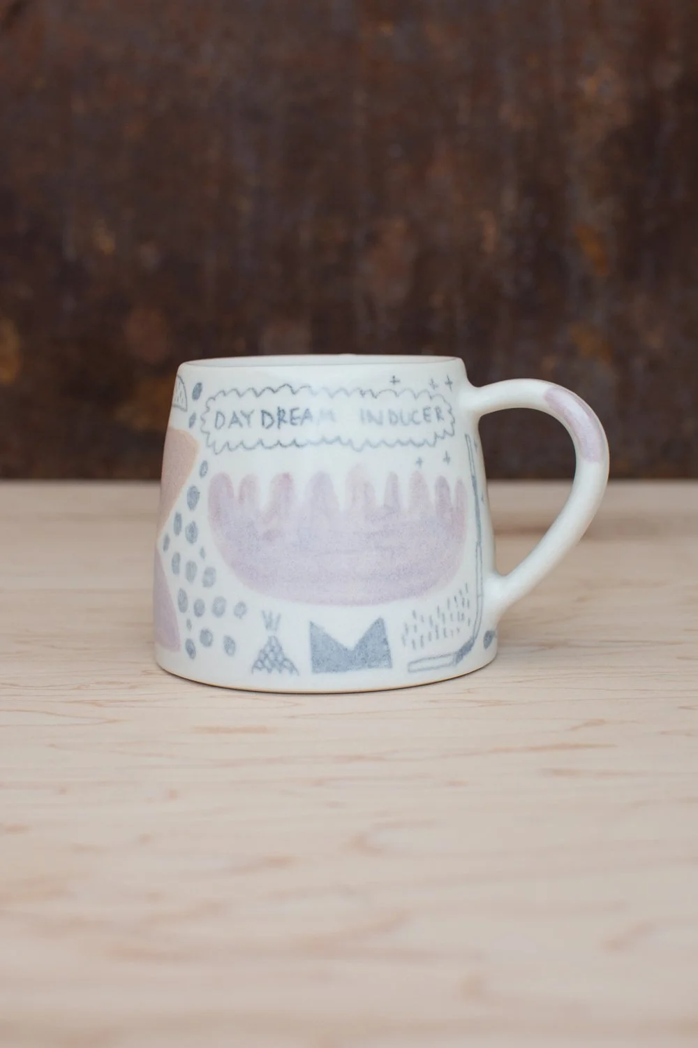Hand-thrown porcelain mug with pink and ochre illustrations.