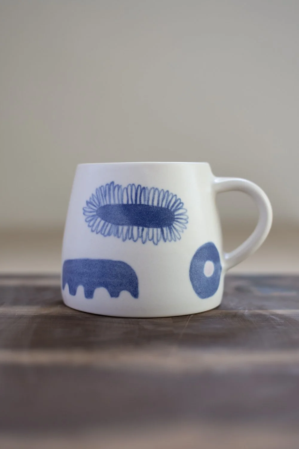 Hand-thrown porcelain mug with blue illustrations painted on the surface.