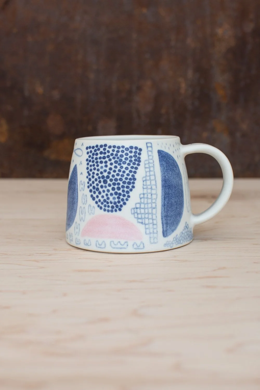 Hand-thrown porcelain mug with blue and pink illustrations painted on the surface.