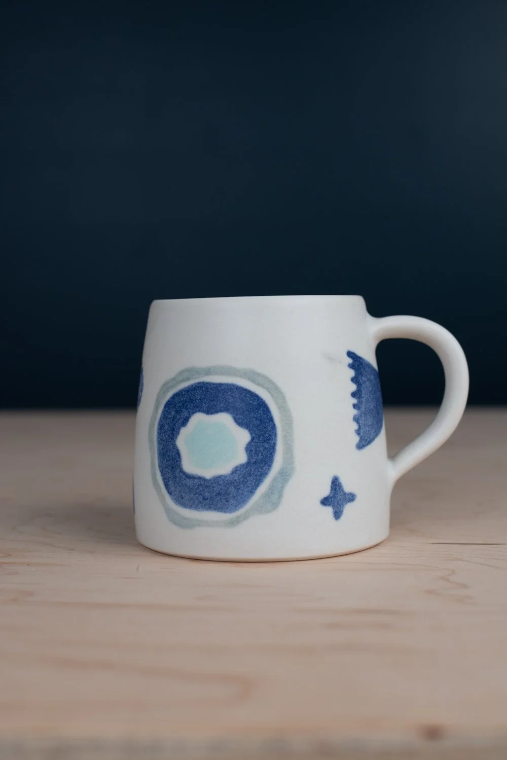 Hand-thrown porcelain mug with blue illustrations painted on the surface.
