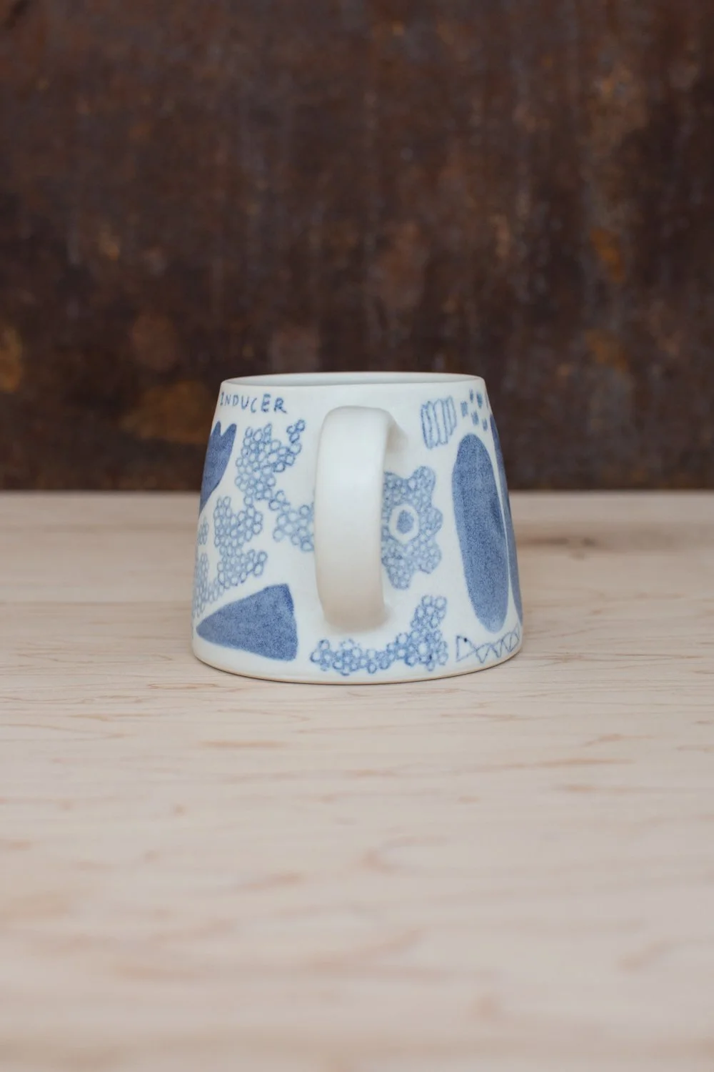 Hand-thrown porcelain mug with blue illustrations painted on the surface.