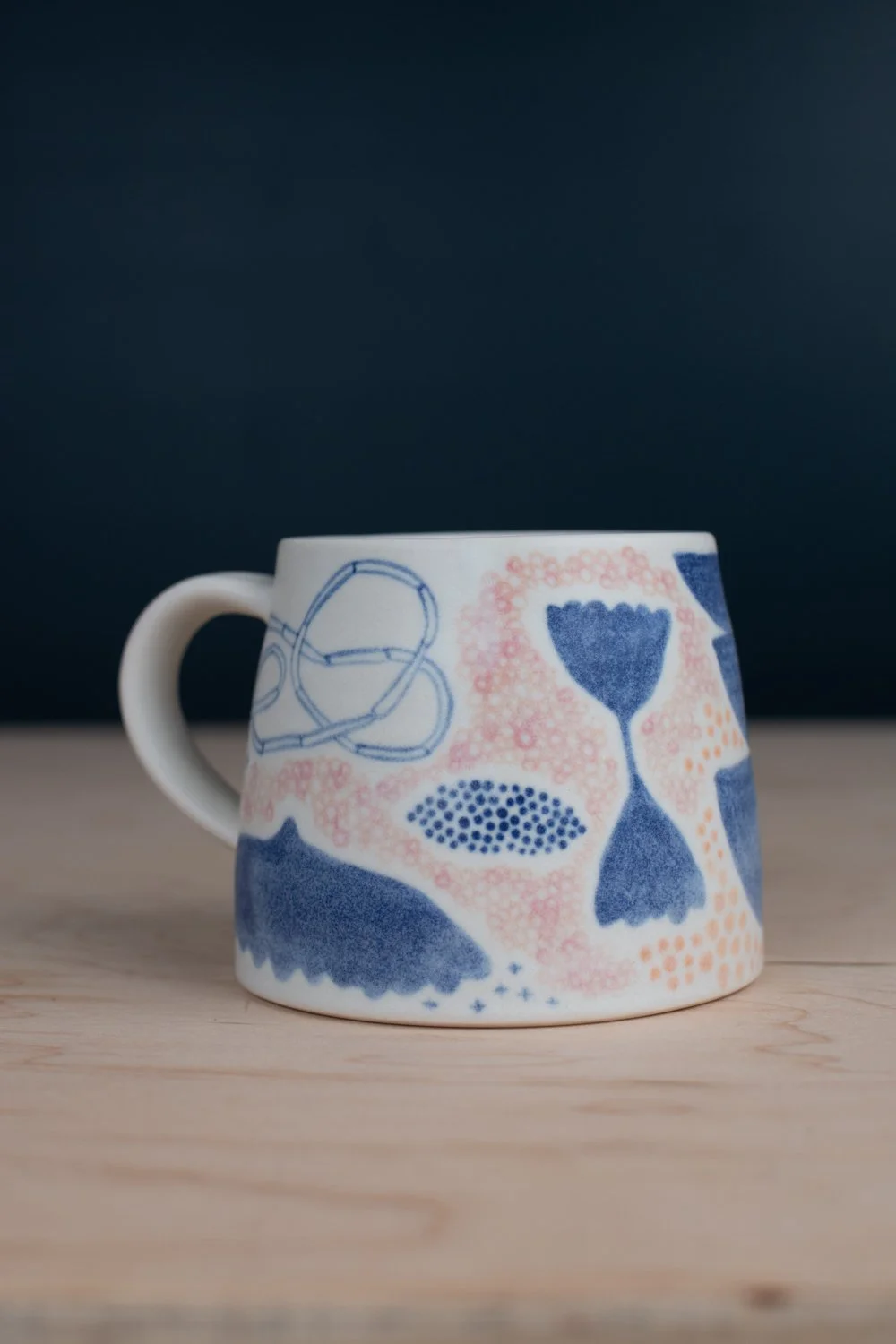 Hand-thrown porcelain mug with blue, blush, and tangerine illustrations painted on the surface.