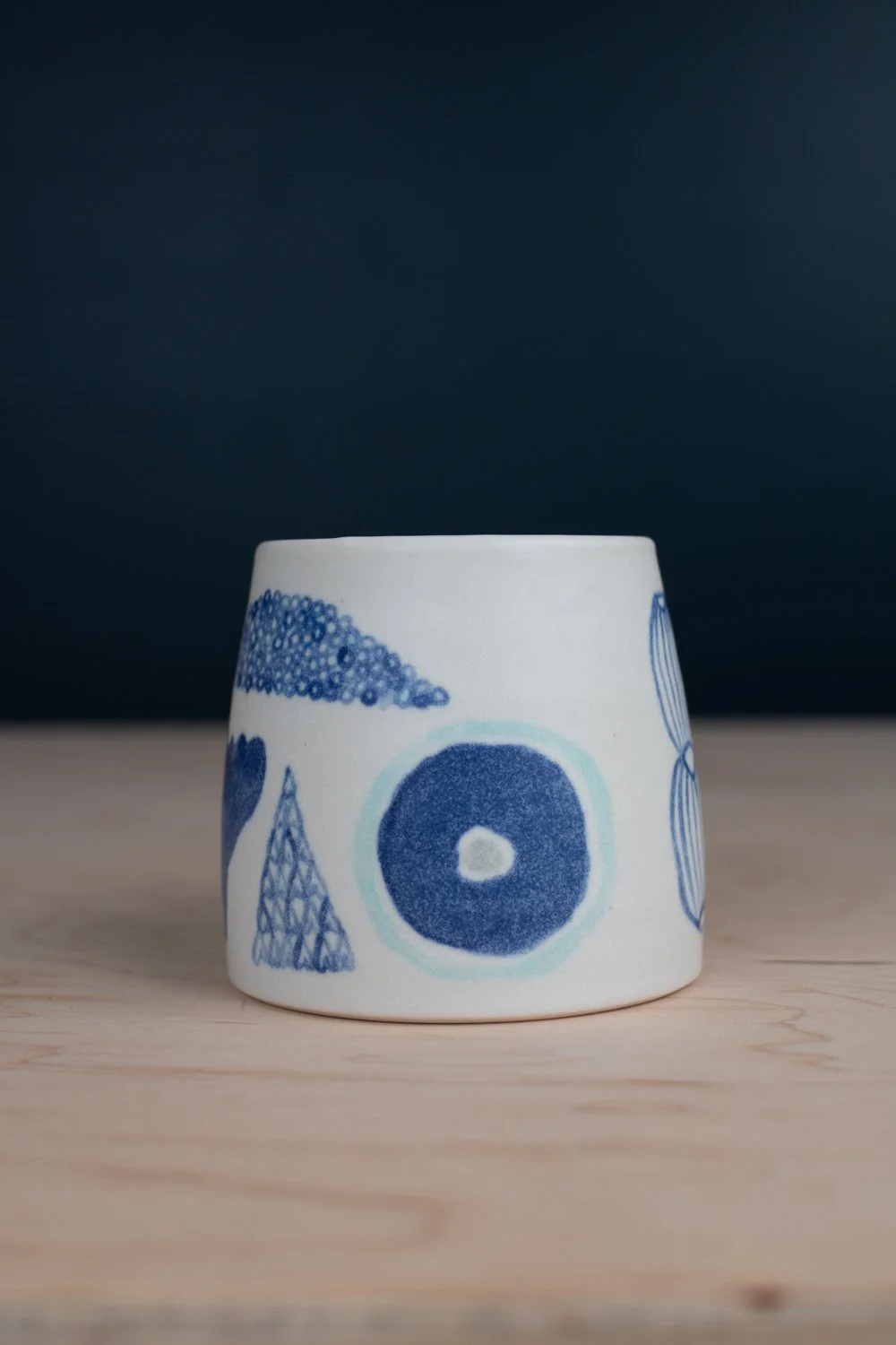 Hand-thrown porcelain mug with blue illustrations painted on the surface.