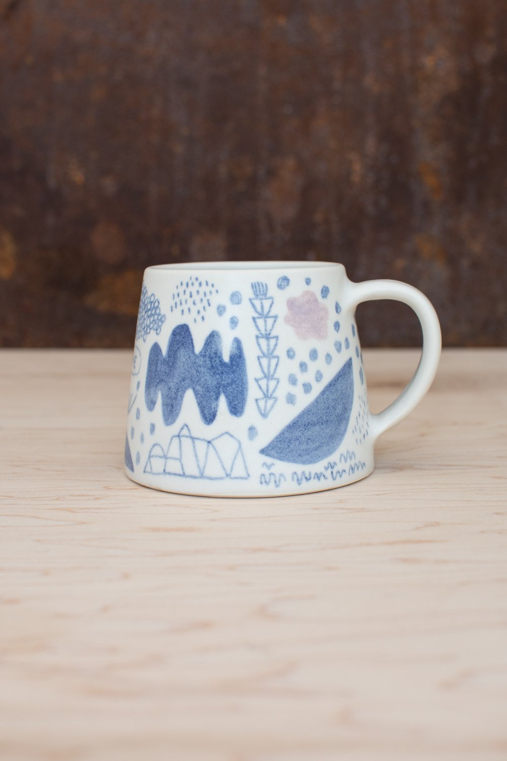 Hand-thrown porcelain mug with blue and pink illustrations.