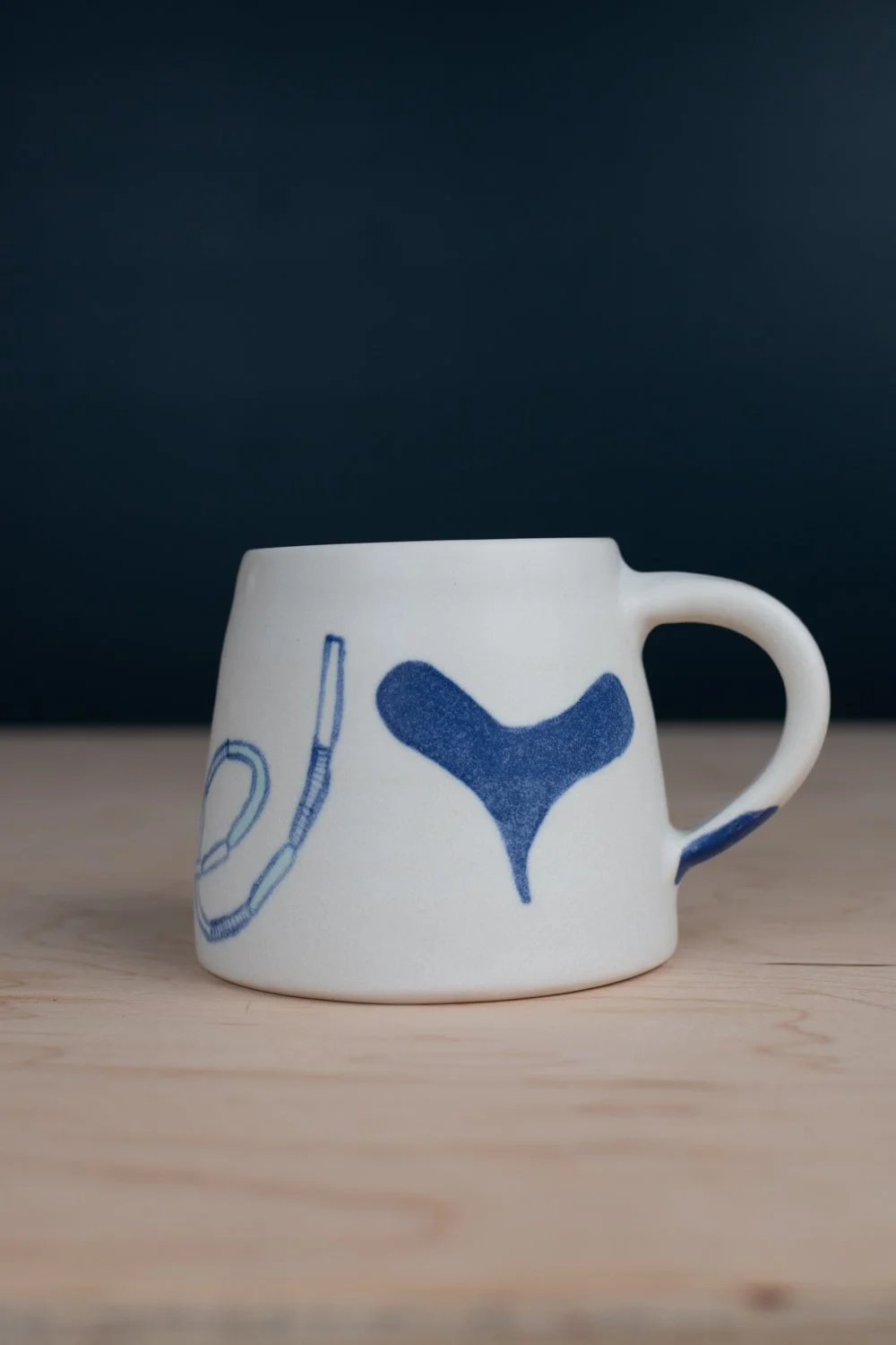 Hand-thrown porcelain mug with blue illustrations painted on the surface.