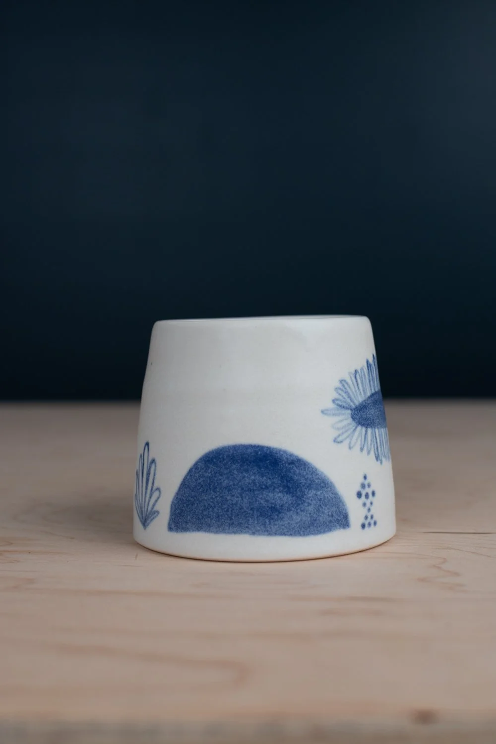 Hand-thrown porcelain mug with blue illustrations painted on the surface.
