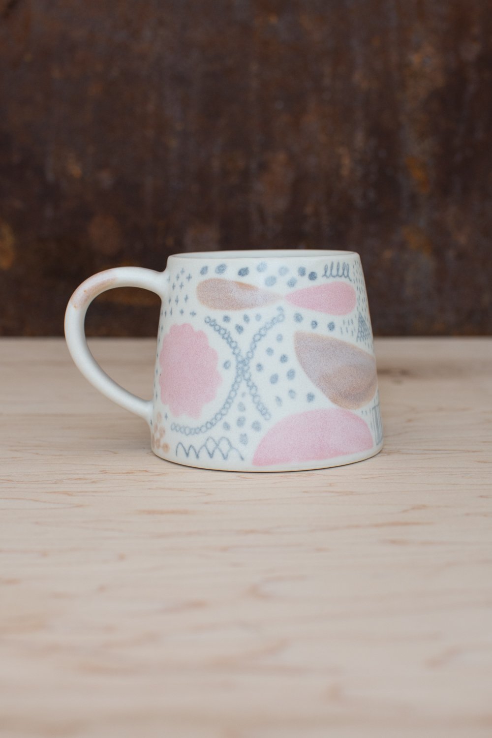 Hand-thrown porcelain mug with pink and ochre illustrations painted on the surface.
